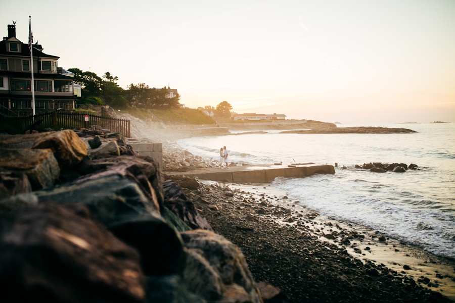 A newly married couple standing together on a New England shoreline at sunrise